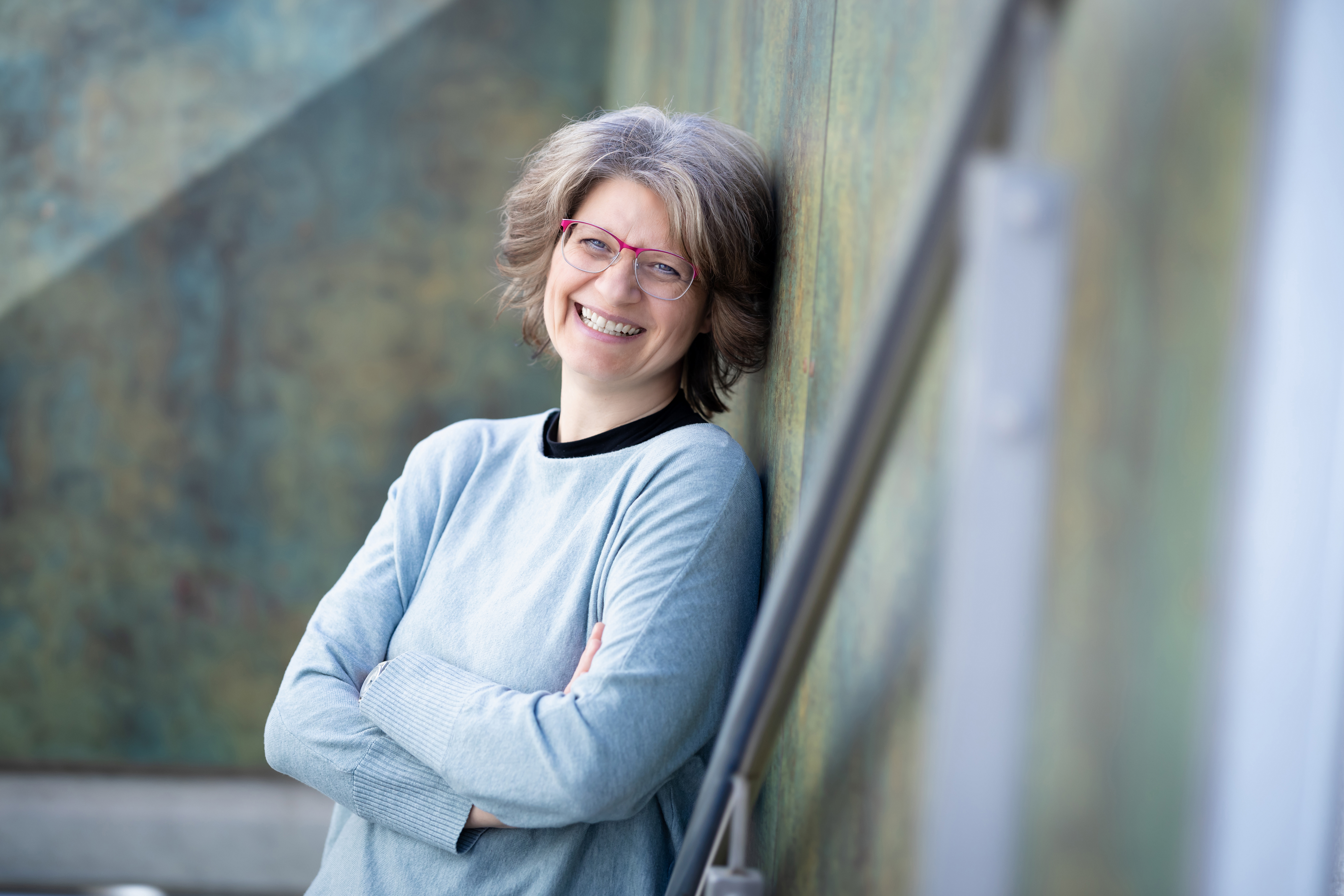 Yvonne Mattner lehnt lächelnd an einer Wand, die Arme locker verschränkt.